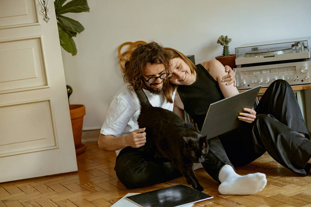 Family couple sitting on floor and listening music on vinyl player with different records - Foto, imagen