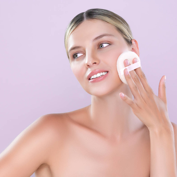 Alluring beautiful female model applying powder puff for facial makeup concept. Portrait of flawless perfect cosmetic skin woman put powder foundation on her face in pink isolated background. - Photo, Image