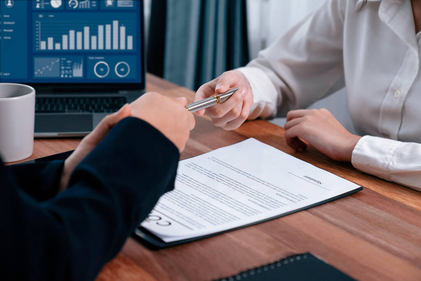 Two businesspeople sit across the desk as business deal is taking place. Corporate attorney handing a pen for client or partner to sign contract paper, sealing the deal with signature. Enthusiastic - Photo, Image