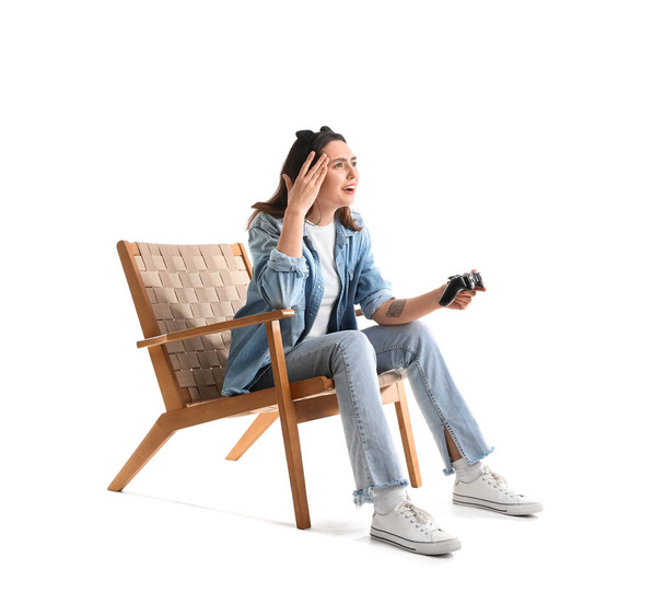 Young woman with headphones playing video game in wooden armchair on white background - Photo, Image