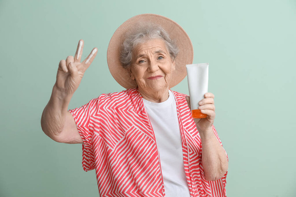 Seniorin mit Sonnencreme zeigt Siegesgeste auf grünem Hintergrund - Foto, Bild