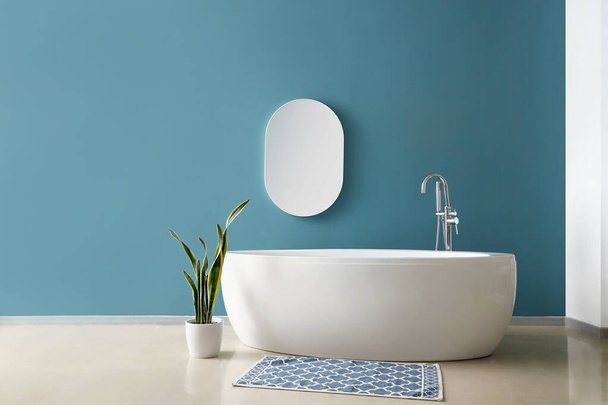 Semplice interno del bagno con vasca, specchio e pianta d'appartamento vicino alla parete blu - Foto, immagini