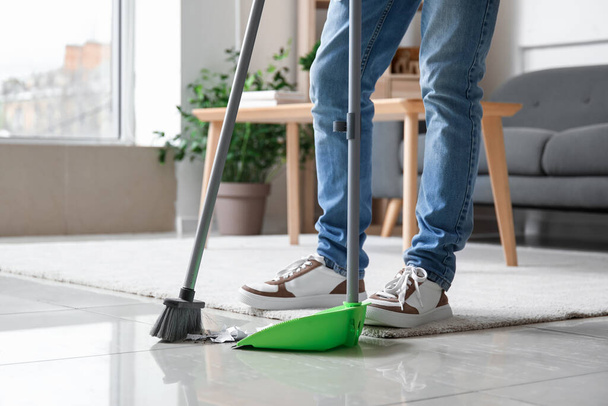 Young man sweeping floor with broom at home - Fotó, kép