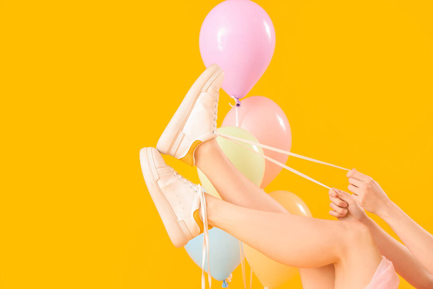 Young woman tying shoes laces with balloons on yellow background - Photo, Image