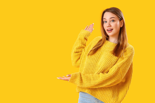 Beautiful young woman showing something on yellow background - Zdjęcie, obraz
