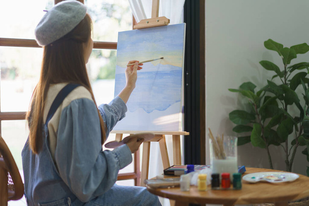 Junge Malerin zeichnet und malt Meisterwerk mit Pinsel auf Leinwand im heimischen Atelier. - Foto, Bild