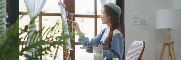 Молодая художница использует кисть для рисования и живописи шедевра на холсте в домашней студии. - Фото, изображение