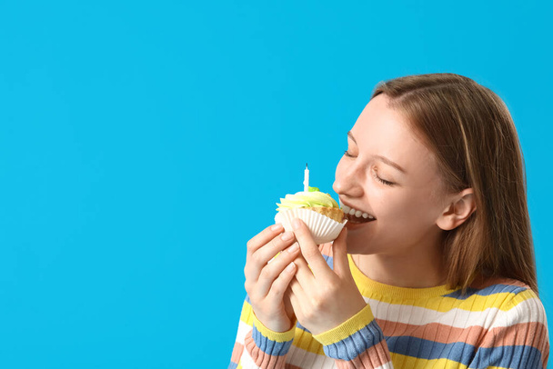 Beautiful young woman eating tasty birthday cake on blue background - Foto, Imagen