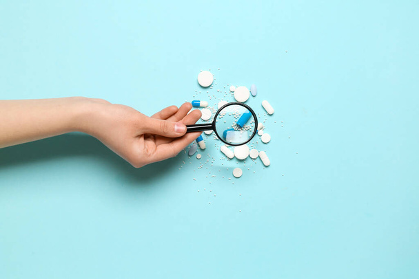 Female hand with magnifier and pills on blue background - Photo, image