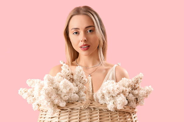 Young woman with basket of lilac flowers on pink background - Foto, afbeelding