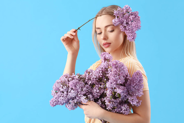 Young woman with lilac flowers on blue background - Valokuva, kuva