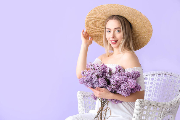 Young woman with lilac flowers in armchair on color background - Photo, Image