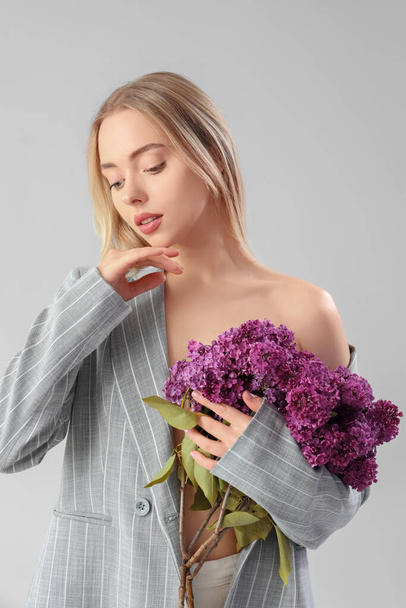 Young woman with lilac flowers on light background - Foto, afbeelding