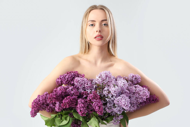 Naked young woman with lilac flowers on light background - Photo, Image