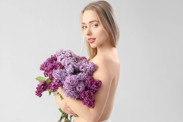 Naked young woman with lilac flowers on light background - 写真・画像