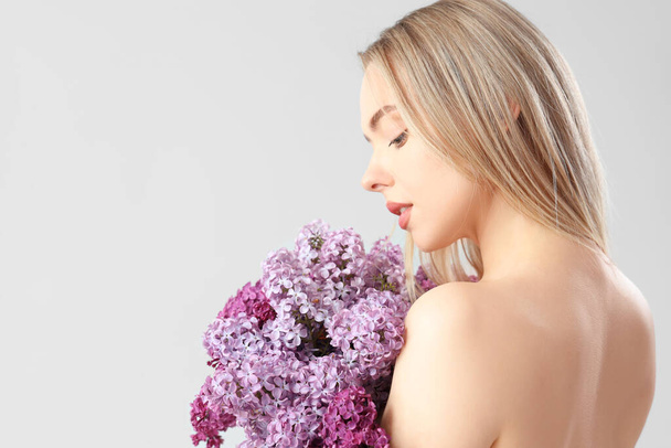Naked young woman with lilac flowers on light background, closeup - Foto, Bild