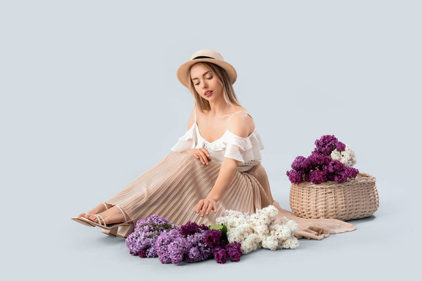 Young woman with lilac flowers on light background - Fotoğraf, Görsel
