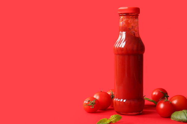 Glasflasche Ketchup und Tomaten auf rotem Hintergrund - Foto, Bild