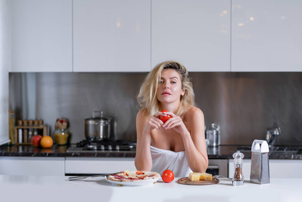 Woman with ingredients for pizza, cheese, sausage and tomato. Woman eating breakfast in a kitchen. Sexy housewife on morning. Housework - Φωτογραφία, εικόνα