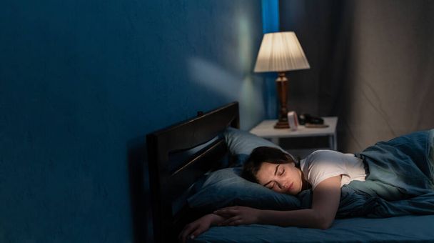Fiatal nő, aki puha ágyban alszik késő éjjel. Feküdni kényelmesen az ágyban, átölelni egy párnát. A lány alszik éjszaka. Fénymásolási hely - Fotó, kép
