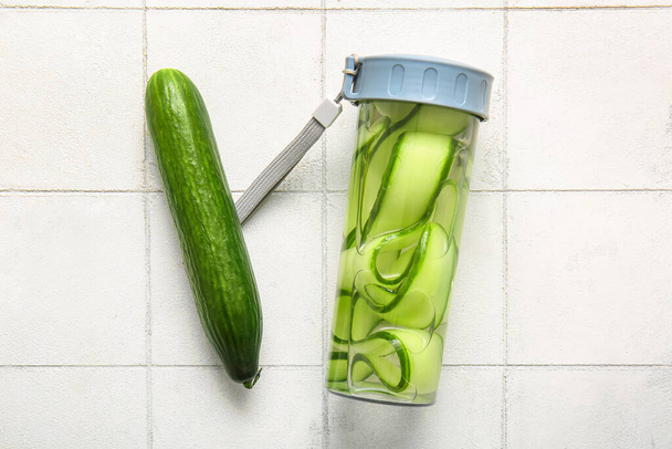 Sports bottle of infused water with cucumber slices on white tile background - Фото, зображення