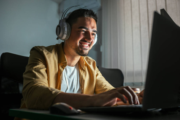 Un joven que trabaja hasta tarde en la oficina. Un hombre está sentado en una laptop en una oficina oscura - Foto, Imagen