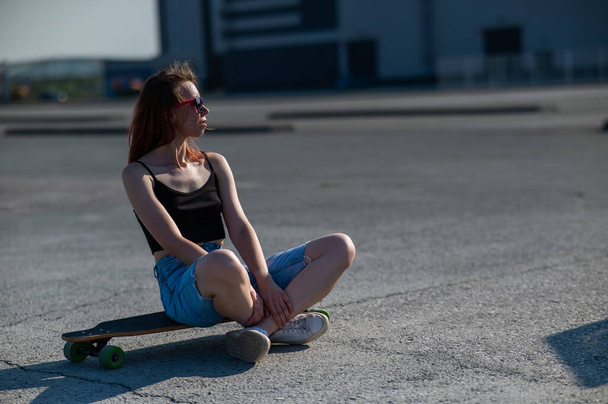 Young caucasian woman sitting on a longboard and relaxing outdoors - Фото, зображення