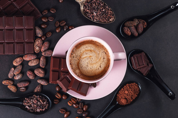 Aromatische Cappuccino-Kaffeetasse mit Kaffeebohnen, Schokoriegel, Kakaofedern auf schwarzem Hintergrund - Foto, Bild
