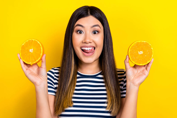 Portrait of japanese young woman wear striped t-shirt hold orange fruits lick teeth tongue summertime isolated on yellow color background. - Φωτογραφία, εικόνα