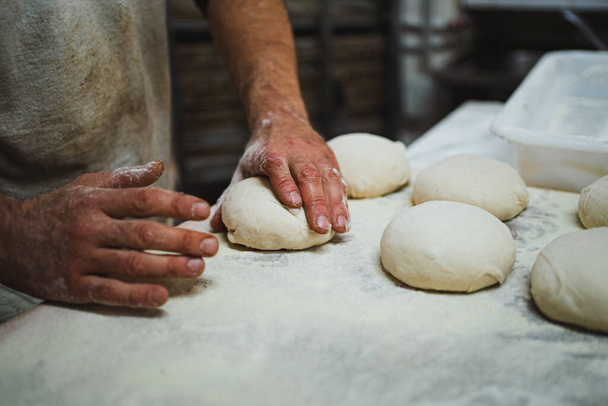 Anonymous baker preshaping bread dough in bakery. He is kneading it. - Zdjęcie, obraz