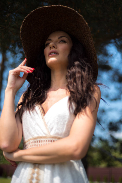 a young girl with a long hair in a black dress and white hat posing on the grass  - Foto, Imagem