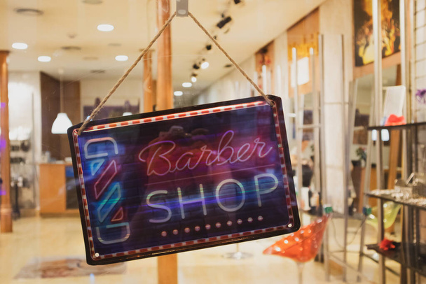 Černá dřevěná cedule s textem 'Barber Shop' na skleněných dveřích kadeřnického salonu krásy pro muže. Ostříhání, koncepce péče o vlasy. Obchodní koncept. Staromódní pruhovaný holičský tyč.  - Fotografie, Obrázek