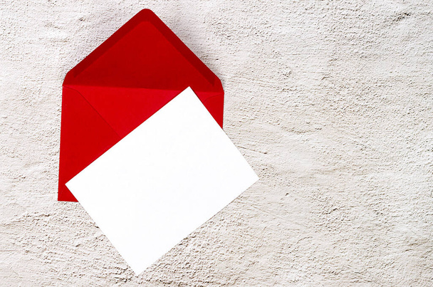 Red envelope with empty white card for text on grey concrete background. Blank invitation or greeting card mockup with copy space - Fotó, kép