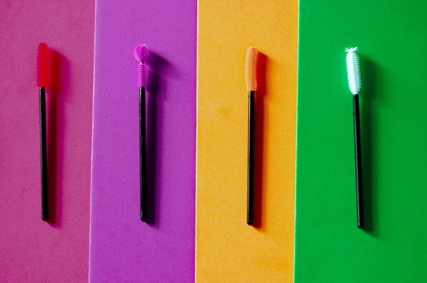Set di pennelli mascara in silicone multicolore su uno sfondo luminoso multicolore. Spazzole verdi, rosa, viola, arancioni. Cosmetici decorativi moderni per donne. Bellezza femminile e moda glamour.  - Foto, immagini