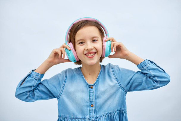 Girl teenager in casual denim dress listening to music in headphones on white background, wireless earphones enjoying music dancing , Modern technology, Protect Developing Ears - Foto, Imagem