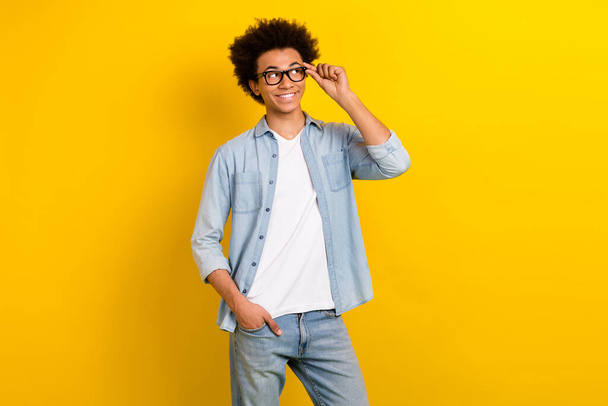 Photo of thoughtful dreamy guy dressed denim shirt arm hand eyewear looking empty space isolated yellow color background. - Фото, изображение
