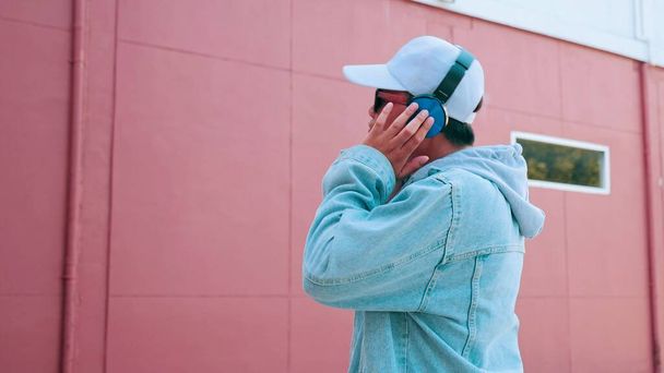 Vrolijke jonge aziatische man in spijkerbroek draagt een koptelefoon luisteren naar muziek genieten van favoriete nummer. Levensstijl en geluksconcept - Foto, afbeelding