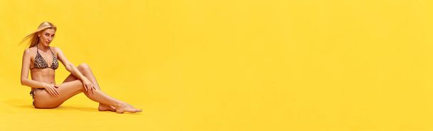 Hermosa mujer joven con perfecto, delgado, cuerpo bronceado en traje de baño elegante sobre fondo de estudio amarillo. Concepto de verano, moda, belleza femenina, vacaciones, estilo de vida. Banner. Copiar espacio para anuncio - Foto, imagen