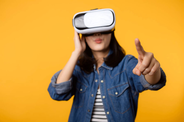 アジアの若い女性は黄色の背景に隔離された仮想現実ヘッドセットゲームエンターテイメントを身に着けて経験を積む。サイバー未来のビデオゲームのコンセプトの勝者. - 写真・画像