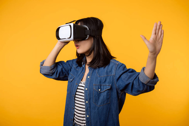 Asian young woman happy success wearing virtual reality headset game entertainment isolated on yellow background. Winner of cyber future video game concept. - 写真・画像