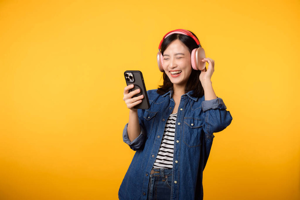 Portré fiatal vidám ázsiai nő élvezze hallgatni audio okostelefon zenei alkalmazás ellen sárga. Boldog mosolygó női személy fülhallgatóval. Hang, szabadidő, életmód, technológiai koncepció - Fotó, kép