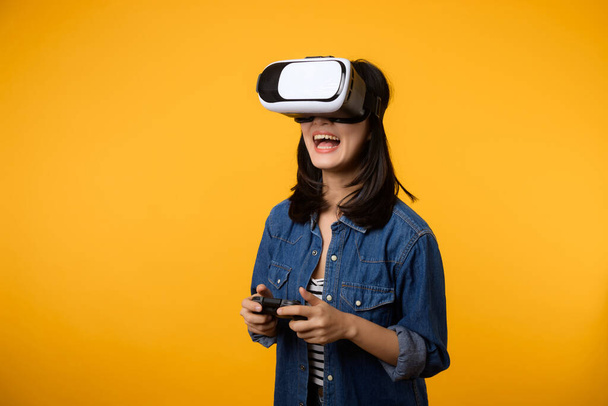 Aziatische jonge vrouw gelukkig succes met het dragen van virtual reality headset game entertainment en houden joystick controller geïsoleerd op gele achtergrond. Winnaar van cyber toekomstige video game concept. - Foto, afbeelding