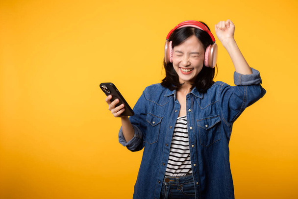 Portre genç, neşeli Asyalı kadın sarıya karşı akıllı telefon müzik uygulaması ile ses dinlemeyi seviyor. Kulaklıklı, mutlu, gülümseyen bir kadın. Ses, eğlence, yaşam tarzı, teknoloji konsepti - Fotoğraf, Görsel