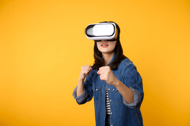 Asiatique jeune femme obtenir expérimenté portant réalité virtuelle jeu de casque divertissement isolé sur fond jaune. Gagnant du concept de cyberfutur jeu vidéo. - Photo, image