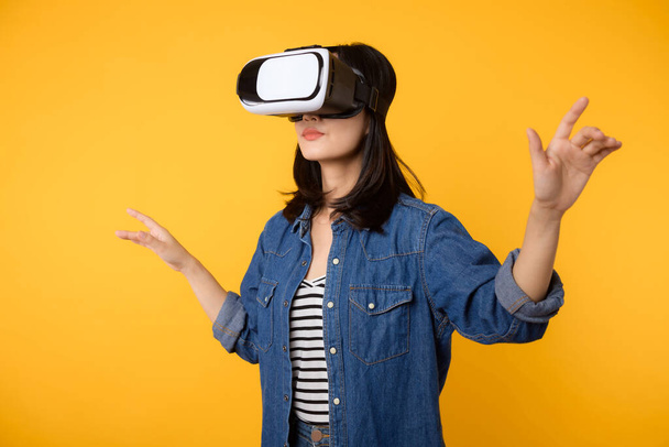 Ázsiai fiatal nő kap tapasztalt visel virtuális valóság headset játék szórakozás elszigetelt sárga alapon. A kiber jövő videojáték koncepciójának nyertese. - Fotó, kép
