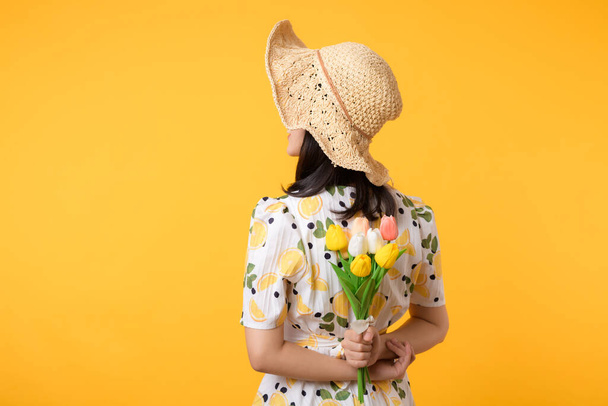 Studioporträt hübsche junge asiatische Frau glücklich lächeln Dressing Frühlingsmode mit Hut hält Tulpenstrauß Blume vor gelbem Studiohintergrund. Personenfreizeitkonzept. - Foto, Bild