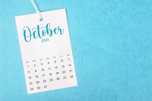 2023 October calendar page hanged on white rope  on blue background. - Фото, изображение