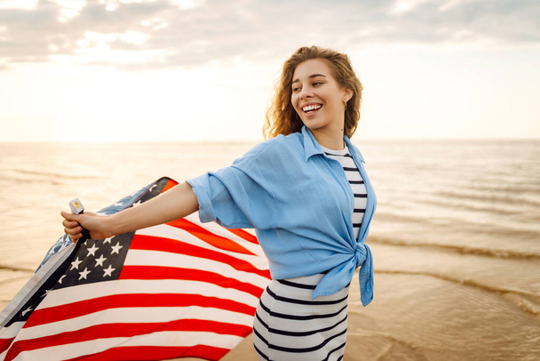 Mladá žena s americkou vlajkou na pláži. Vlastenecká dovolená. USA slaví 4. července. Koncept Dne nezávislosti - Fotografie, Obrázek