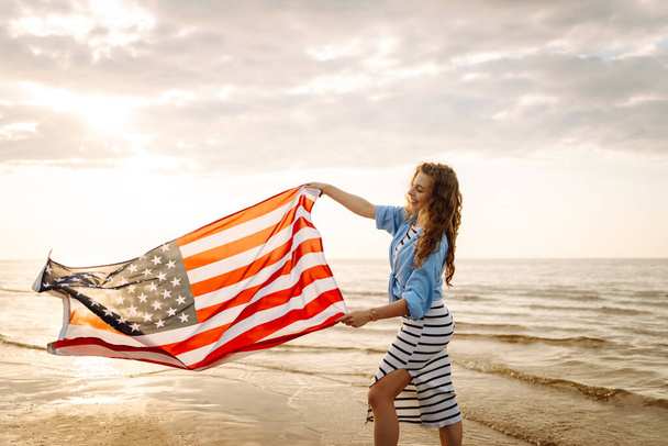 Νεαρή γυναίκα με αμερικανική σημαία στην παραλία. Πατριωτική γιορτή. Οι ΗΠΑ γιορτάζουν την 4η Ιουλίου. Έννοια της ημέρας ανεξαρτησίας - Φωτογραφία, εικόνα