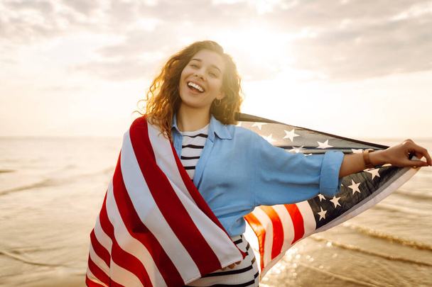Jonge vrouw met Amerikaanse vlag op het strand. Patriottische feestdag. USA vieren 4 juli. Onafhankelijkheidsdag concept - Foto, afbeelding